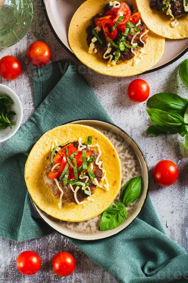 fracasser Burger tacos avec du boeuf petit pâté, tomates et basilic sur une assiette Haut et verticale vue photo