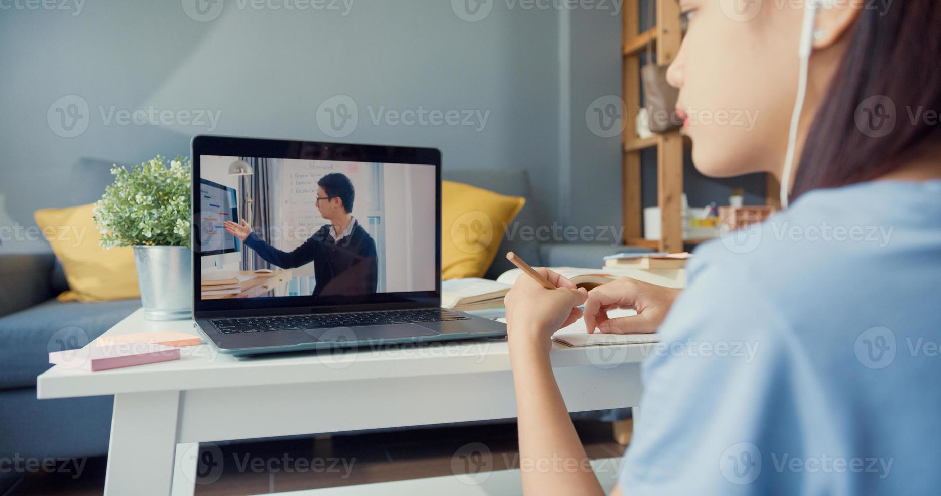 gros plan jeune fille asiatique avec des écouteurs décontractés utilise un appel vidéo sur ordinateur portable apprend en ligne avec un tuteur dans le salon de la maison. isoler le concept de pandémie de coronavirus d'apprentissage en ligne de l'éducation en ligne. photo