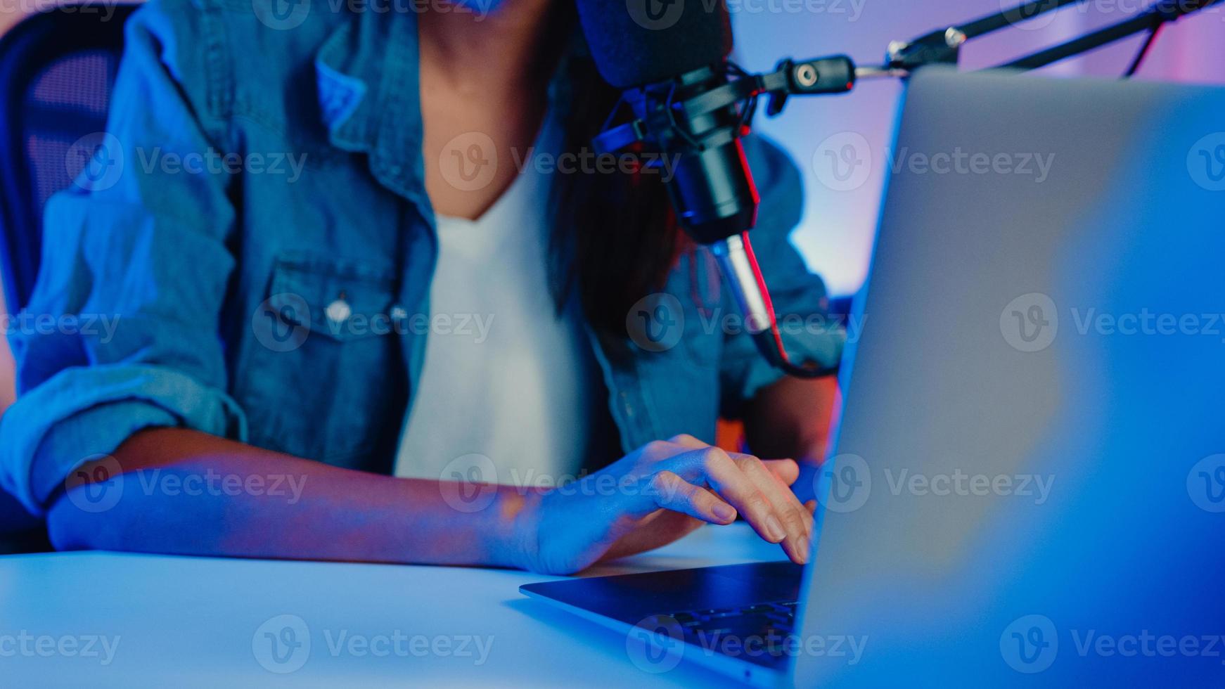 Happy asia girl host record podcast utiliser un microphone porter un casque avec un ordinateur portable interviewer une conversation d'invité pour le contenu dans son home studio la nuit. concept d'équipement sonore. concept de créateur de contenu. photo