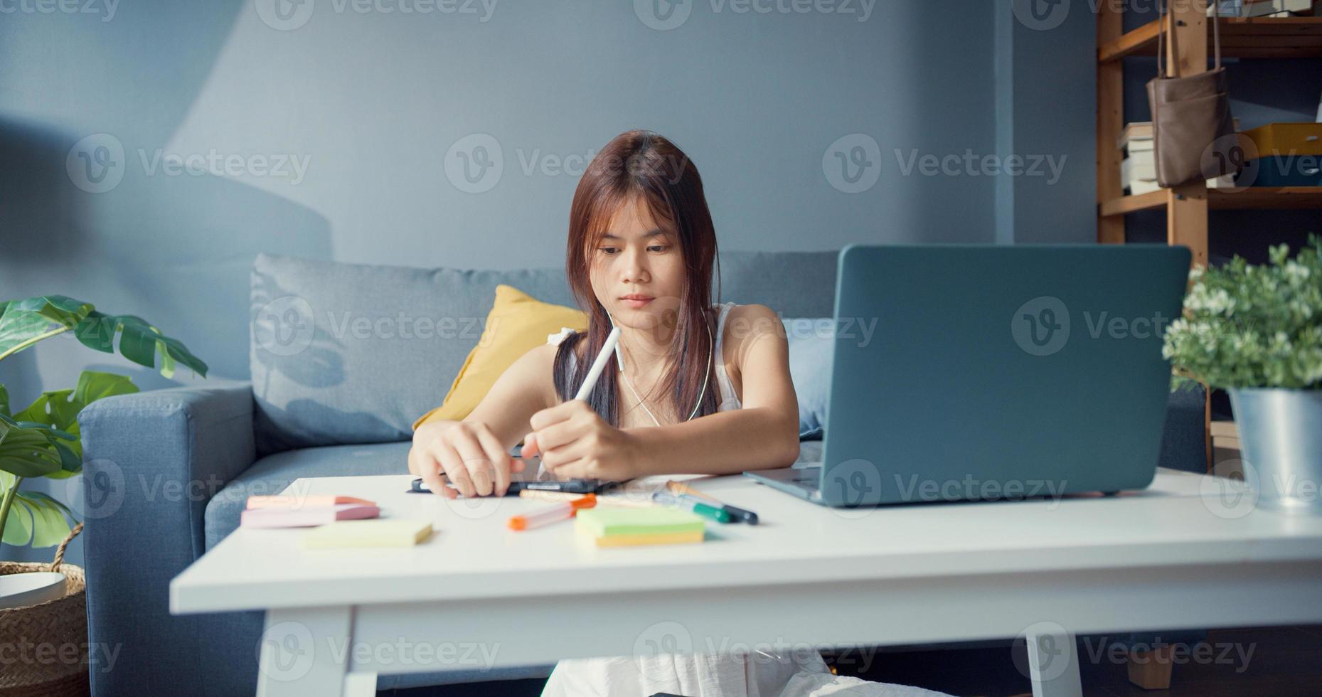 jeune fille asiatique adolescente avec chemise décontractée porter des écouteurs utiliser un ordinateur portable apprendre en ligne écrire une conférence dans un ordinateur portable dans le salon de la maison. isoler le concept de pandémie de coronavirus d'apprentissage en ligne de l'éducation en ligne. photo