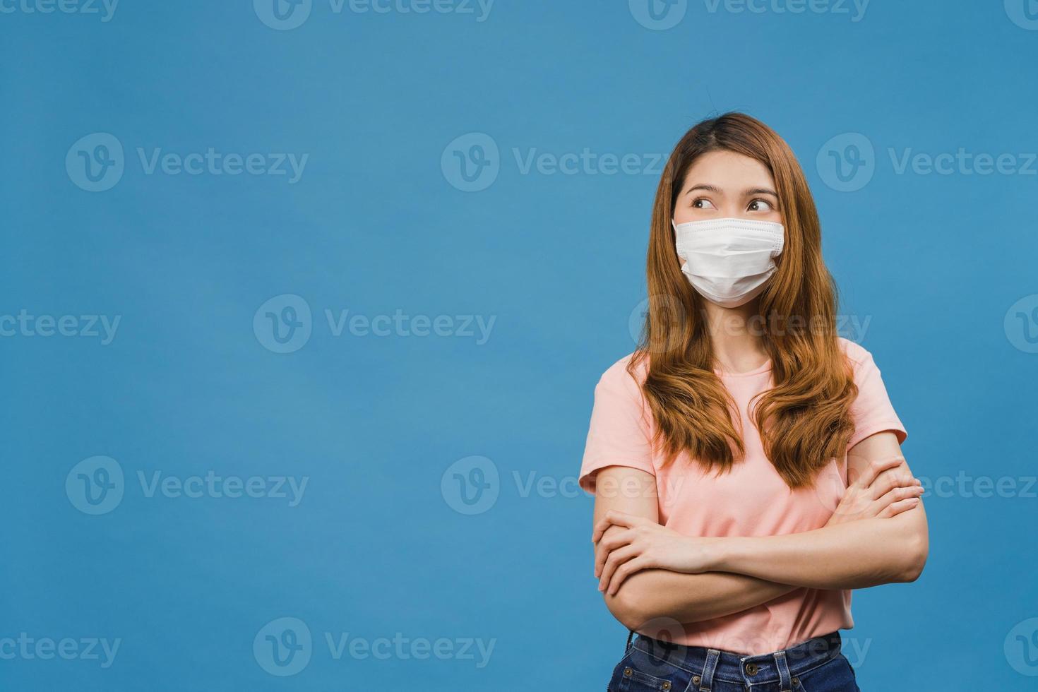 jeune fille asiatique portant un masque médical vêtu d'un tissu décontracté et regardant un espace vide isolé sur fond bleu. auto-isolement, distanciation sociale, quarantaine pour la prévention du virus corona photo