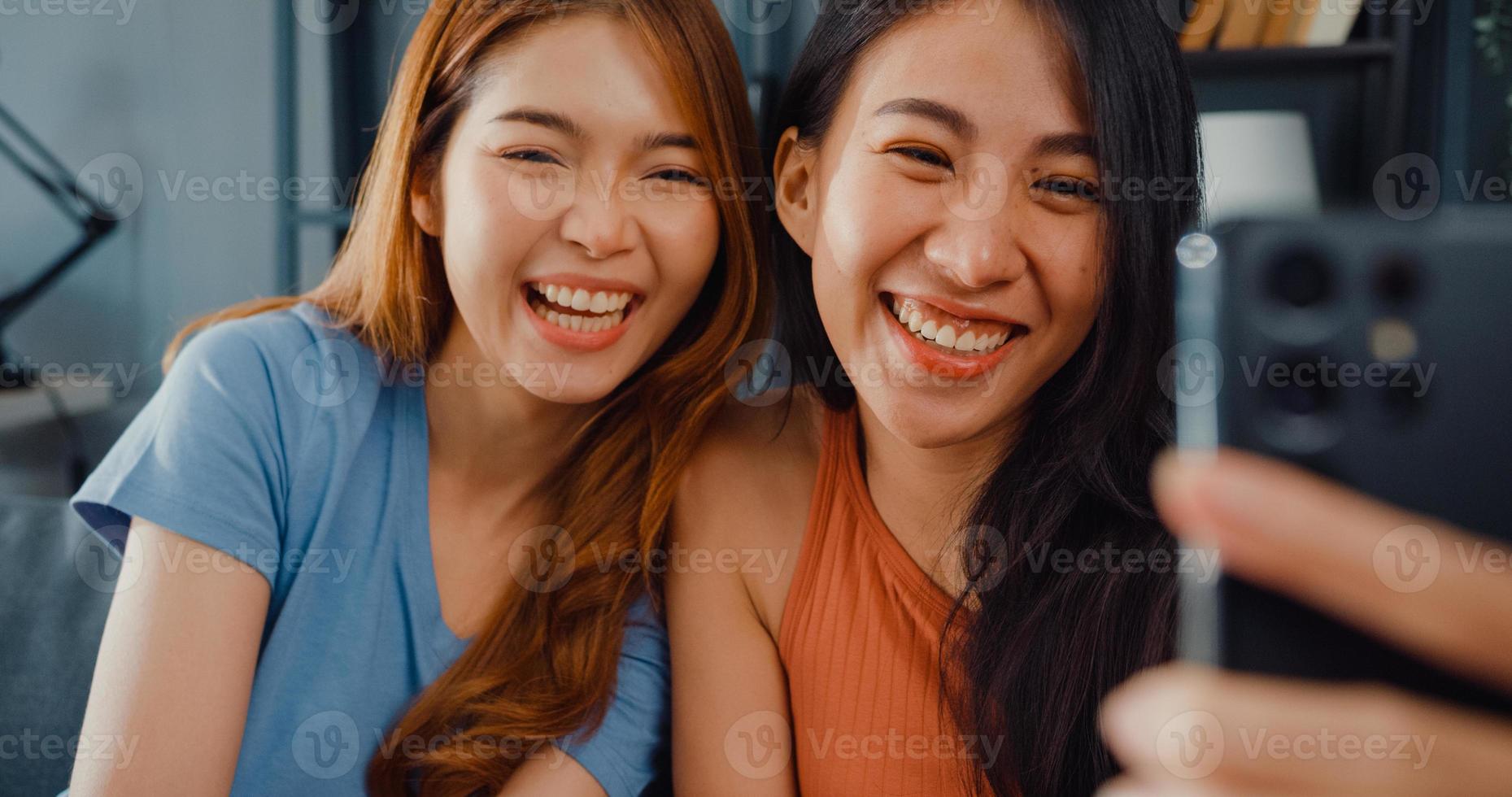 adolescentes asiatiques se sentant heureuses souriantes se détendent utilisent un appel vidéo sur smartphone dans le salon à la maison. vidéoconférence joyeuse colocataire avec amis et famille, concept de femme de style de vie à la maison. photo