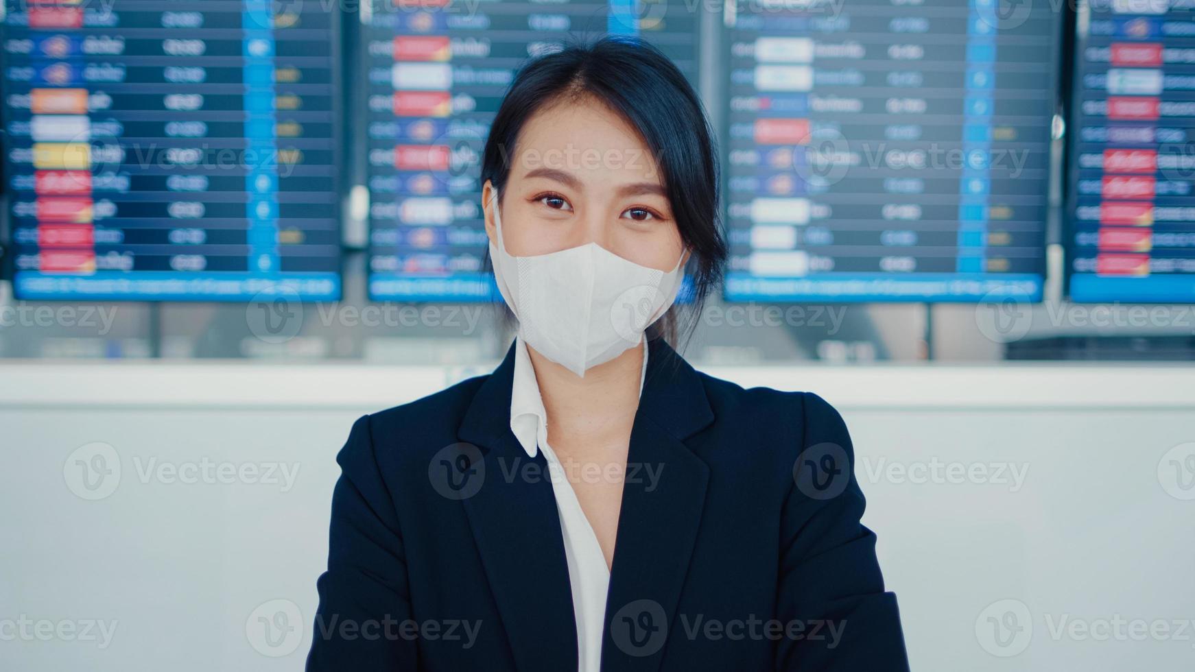 une fille d'affaires asiatique porte un masque facial devant l'heure du spectacle de vol à bord, regarde l'aéroport international de la caméra. pandémie de covid de navetteurs d'affaires, distanciation sociale des navetteurs, concept de voyage d'affaires. photo