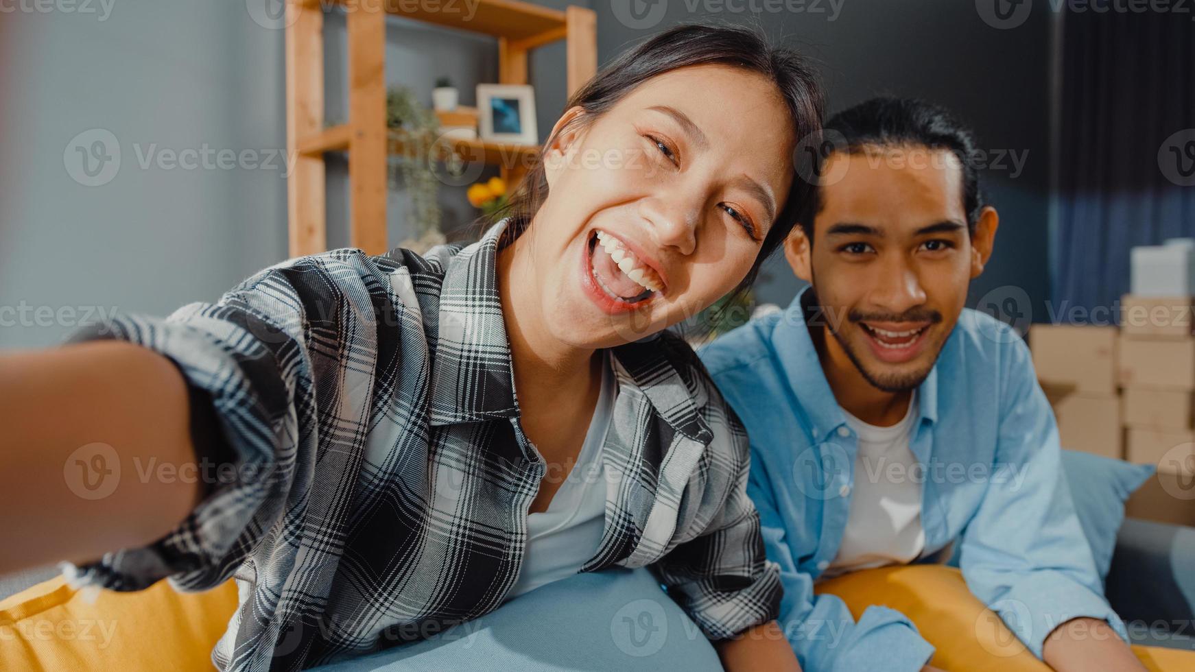 heureux jeune couple asiatique homme et femme assis sur le canapé en regardant l'appel vidéo de la caméra avec des amis et la famille dans le salon à la maison. rester à la maison en quarantaine, distanciation sociale, concept de jeune marié. photo