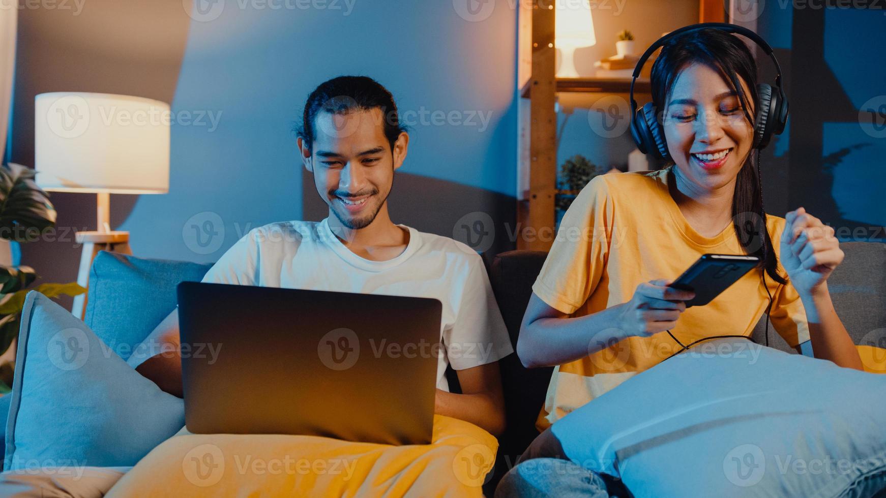 couple d'asie indépendant homme et femme dans un travail décontracté sur un ordinateur portable la nuit profitez d'une détente heureuse avec une femme portez un casque écoutez de la musique sur un smartphone chantez danse sur un canapé à la maison, vie conjugale. photo