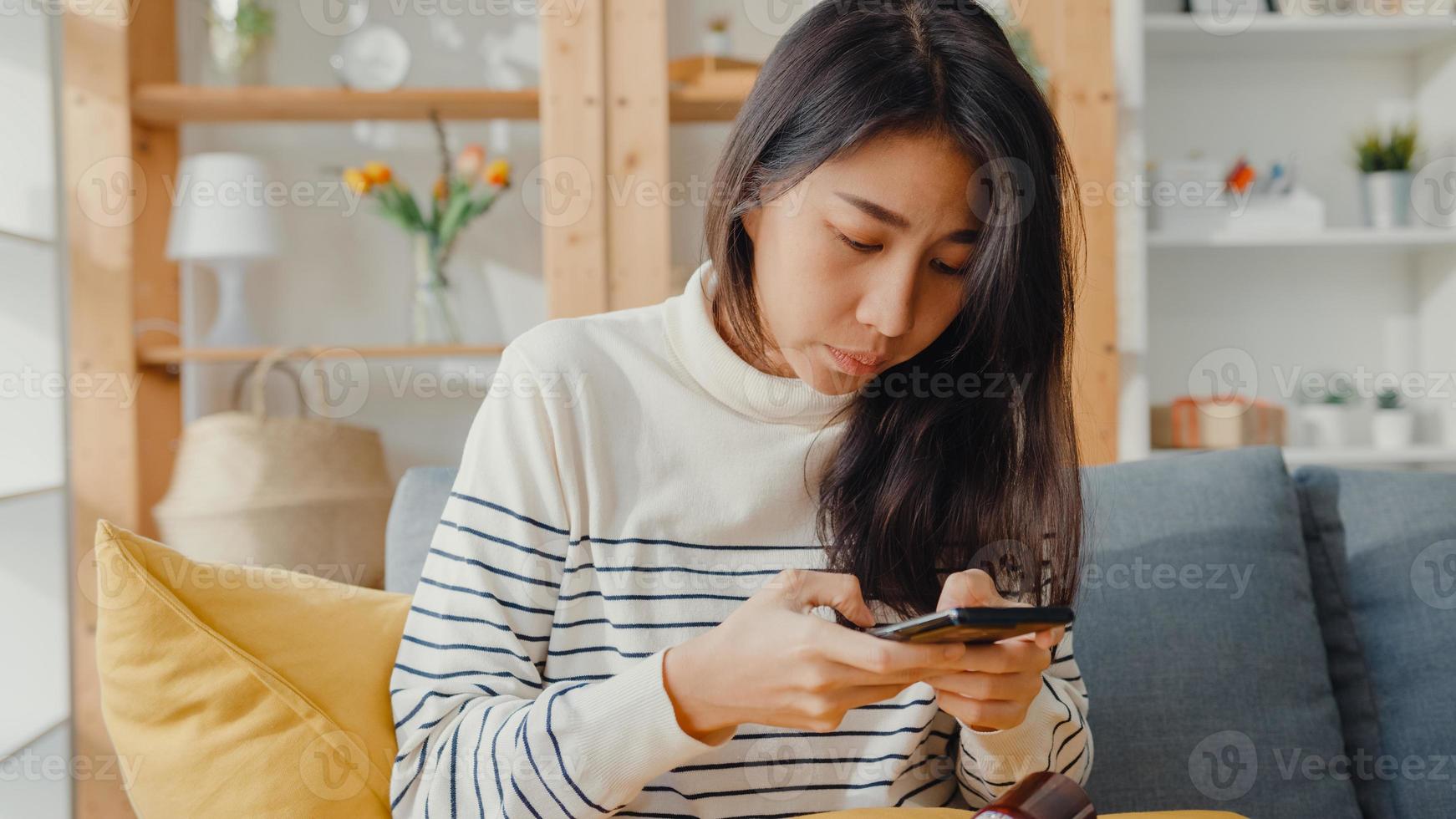 jeune femme asiatique malade tenir un médicament assis sur un canapé prendre une photo envoyée au médecin à la maison. la fille prend des médicaments après l'ordonnance du médecin, mise en quarantaine à la maison, concept de quarantaine de distanciation sociale du coronavirus.