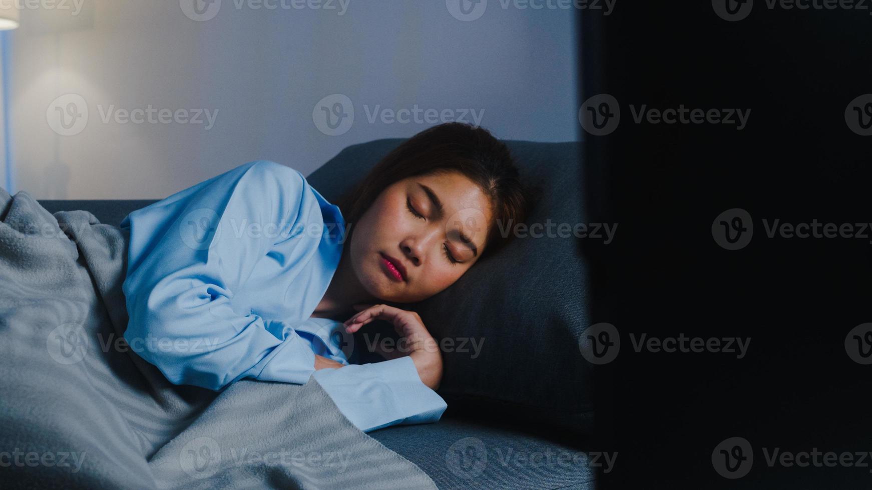 heureuse jeune femme asiatique endormie sur un canapé seule dans le salon tout en regardant un film ou un sport à la télévision tard à la maison le soir. personne qui ronfle, distanciation sociale, quarantaine pour le concept de prévention des coronavirus. photo