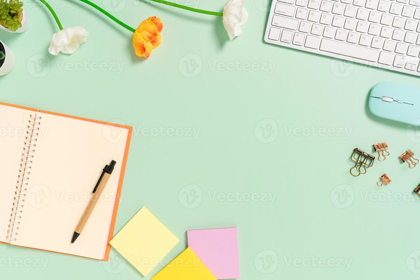 photo créative à plat du bureau de l'espace de travail. bureau vue de dessus avec clavier, souris et bloc-notes noir maquette ouverte sur fond de couleur vert pastel. vue de dessus maquette avec copie espace photographie.