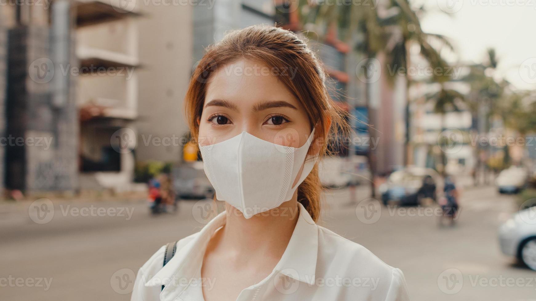 Une jeune femme d'affaires asiatique réussie dans des vêtements de bureau de mode porte un masque médical souriant et regardant la caméra tout en étant heureuse seule à l'extérieur dans une ville urbaine moderne. concept d'entreprise en déplacement. photo