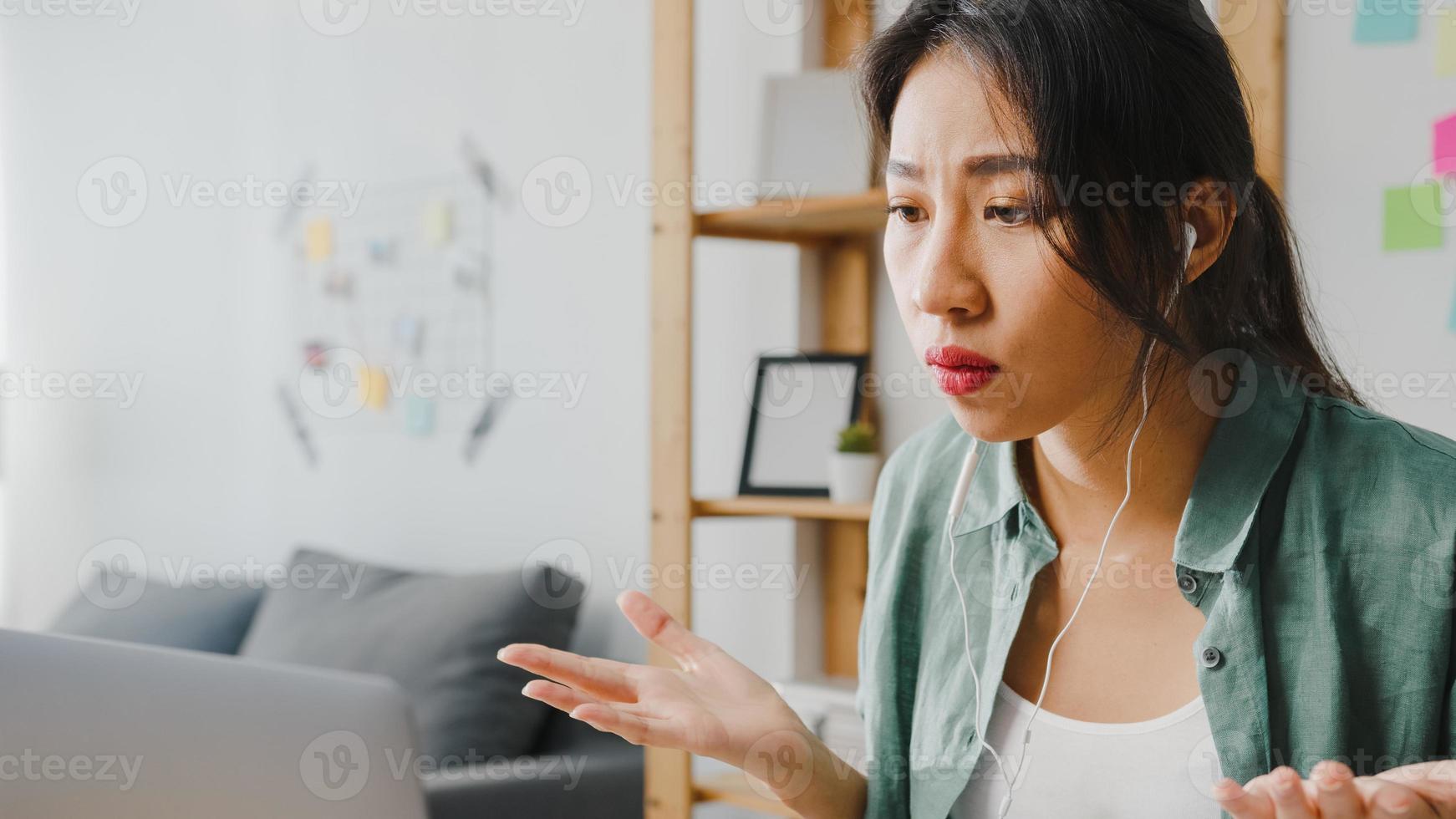 Une femme d'affaires asiatique utilisant un ordinateur portable parle à ses collègues du plan lors d'un appel vidéo tout en travaillant de manière intelligente à domicile dans le salon. auto-isolement, distanciation sociale, quarantaine pour la prévention du virus corona. photo