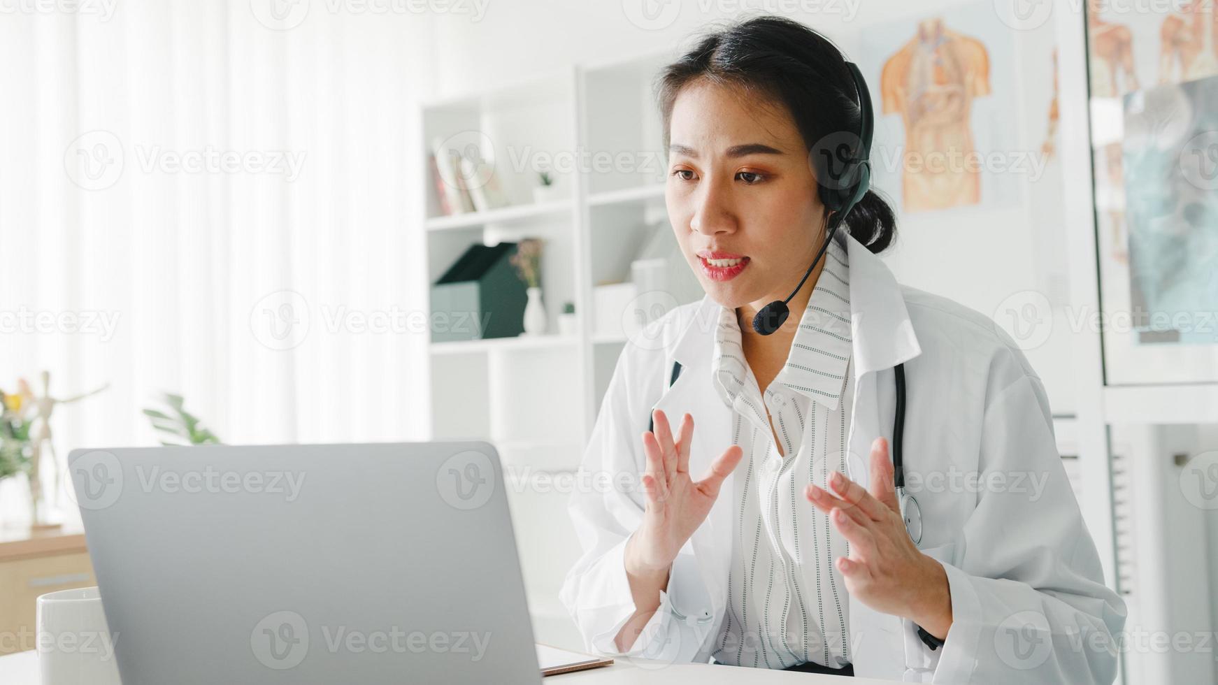 jeune femme médecin asiatique en uniforme médical blanc avec stéthoscope utilisant un ordinateur portable parlant par vidéoconférence avec un patient au bureau dans une clinique de santé ou un hôpital. concept de conseil et de thérapie. photo