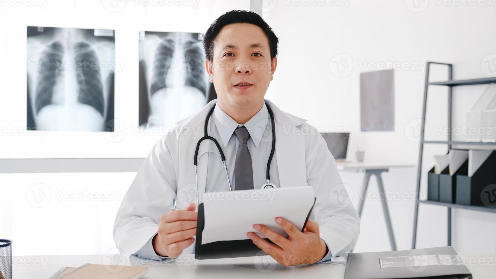 jeune médecin asiatique en uniforme médical blanc avec stéthoscope à l'aide d'un ordinateur portable parler vidéoconférence avec le patient, regardant la caméra dans un hôpital de santé. concept de conseil et de thérapie. photo