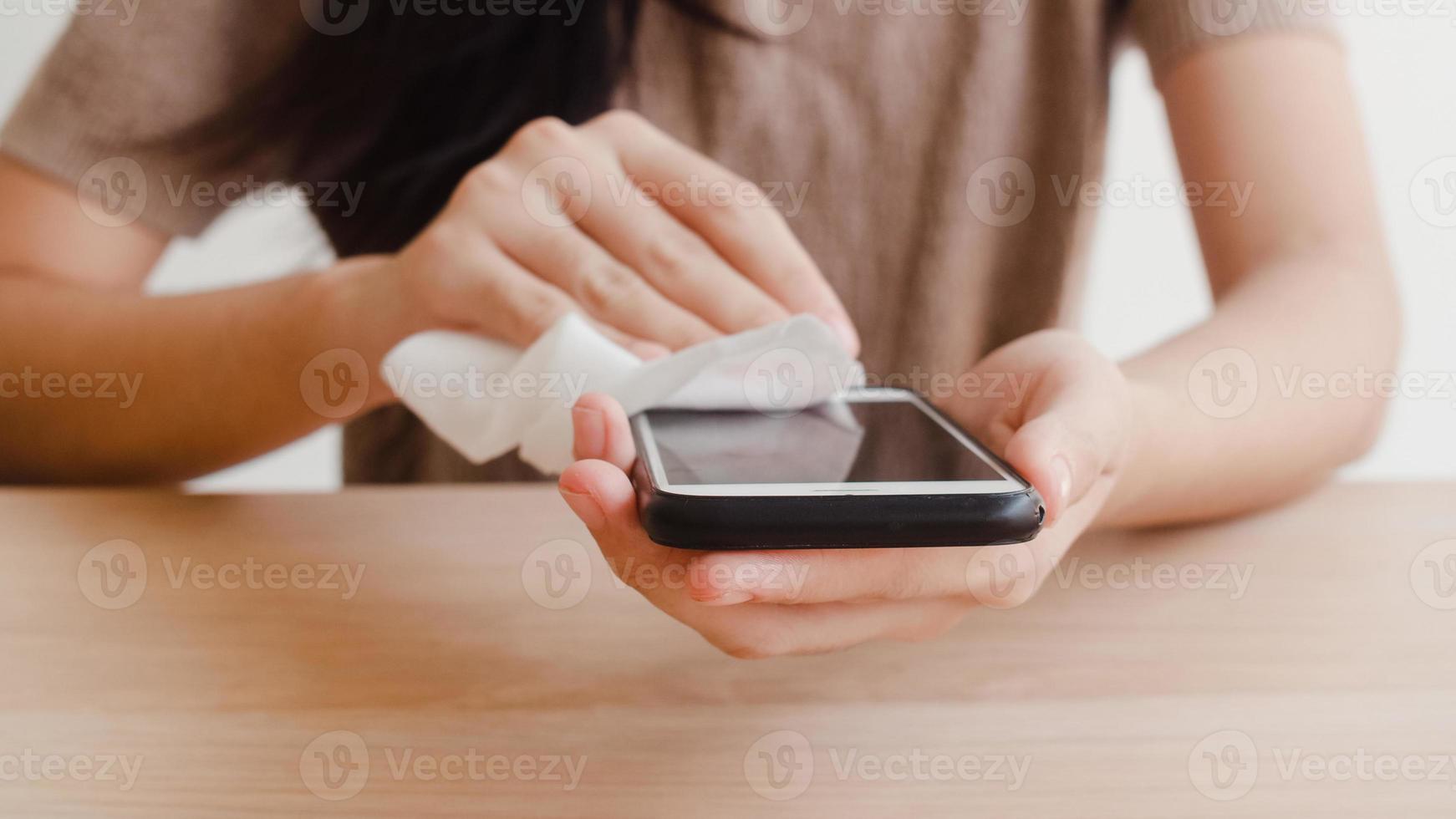 femme asiatique utilisant un spray d'alcool sur un téléphone portable propre avant de l'utiliser pour protéger le coronavirus. surface propre des femmes pour l'hygiène lorsque la distanciation sociale reste à la maison et le temps d'auto-quarantaine. photo