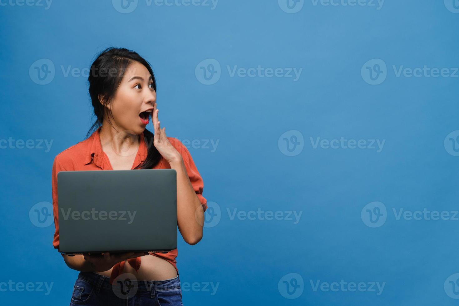 jeune femme asiatique utilisant un ordinateur portable avec une expression positive, sourit largement, vêtue de vêtements décontractés, se sentant heureuse et isolée sur fond bleu. heureuse adorable femme heureuse se réjouit du succès. photo
