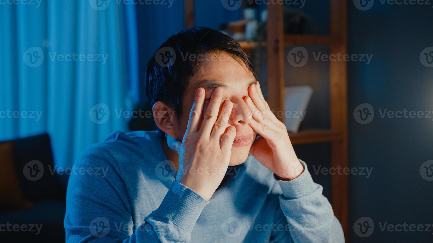 homme d'affaires d'asie faire une pause travailler dur se sentir fatigué détendre les yeux après avoir mis au point un ordinateur de type longue durée dans le salon à la maison des heures supplémentaires la nuit, syndrome du bureau, travail à partir du concept de pandémie corona à domicile. photo