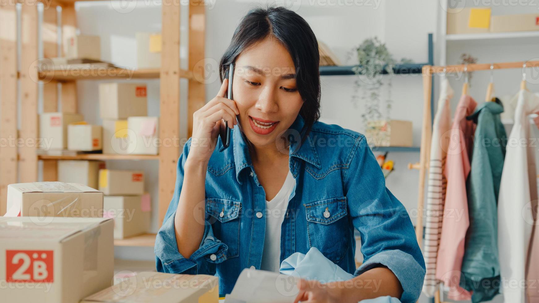 jeune femme d'affaires asiatique utilisant un appel sur smartphone pour recevoir un bon de commande et vérifier le produit en stock au bureau à domicile. propriétaire de petite entreprise, livraison sur le marché en ligne, concept de style de vie indépendant. photo