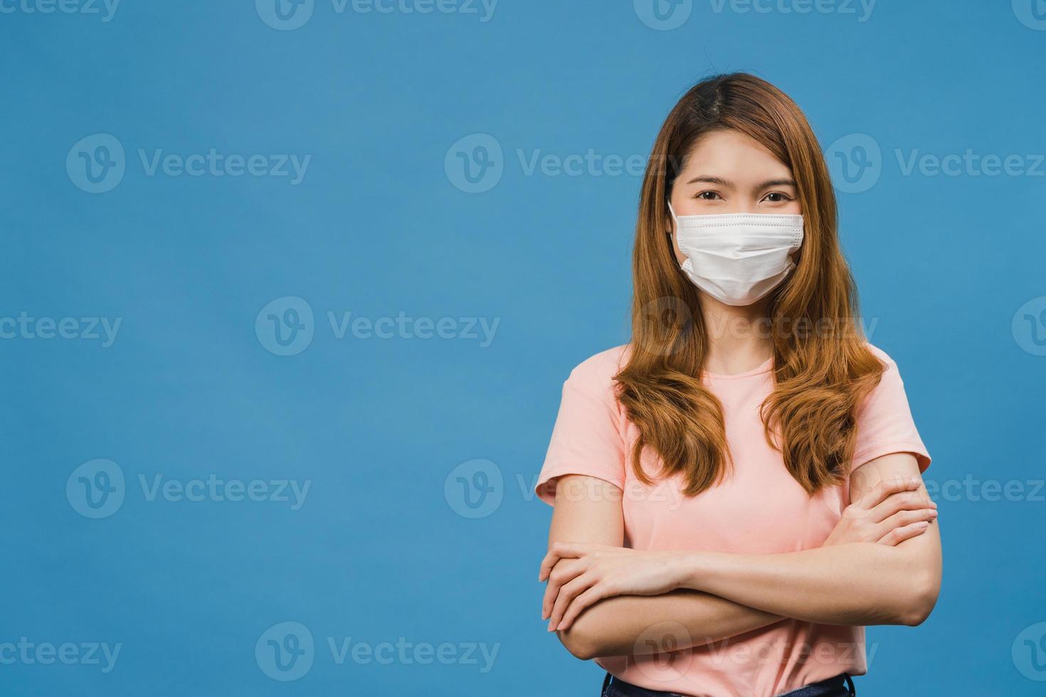 jeune fille asiatique portant un masque médical avec les bras croisés, vêtue d'un tissu décontracté et regardant la caméra isolée sur fond bleu. auto-isolement, distanciation sociale, quarantaine pour le virus corona. photo