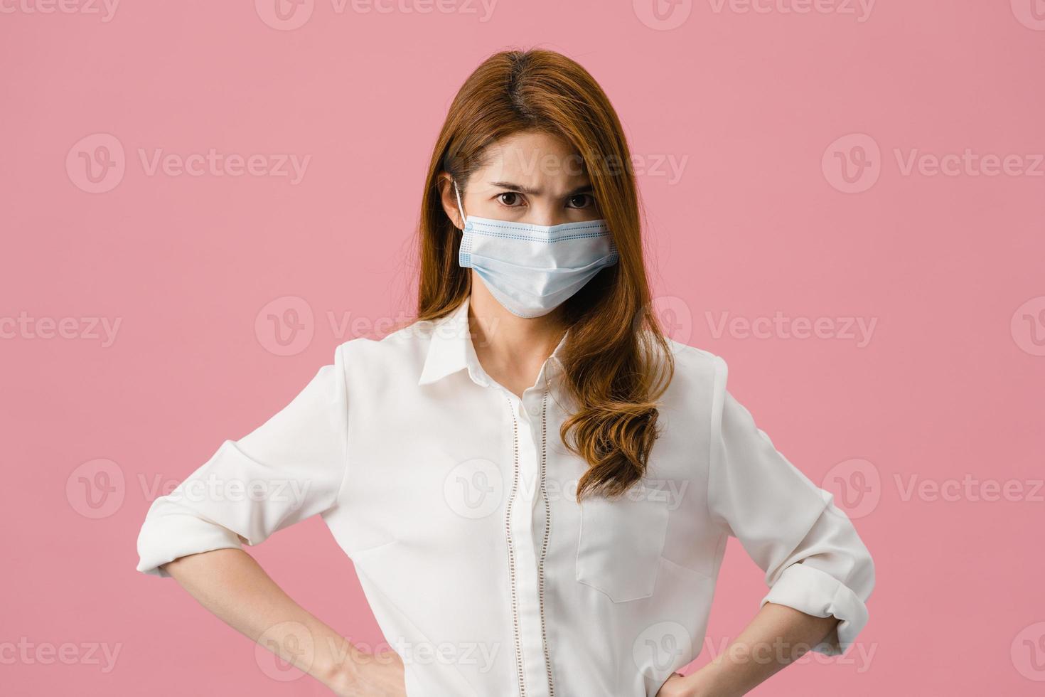 une jeune fille asiatique porte un masque médical avec une expression négative, un cri excité, des pleurs émotionnels en colère et regarde la caméra isolée sur fond rose. distanciation sociale, quarantaine pour le virus corona. photo