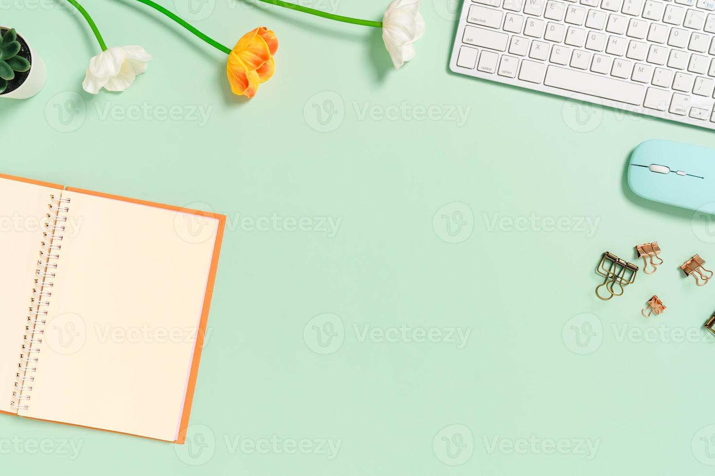 photo créative à plat du bureau de l'espace de travail. bureau vue de dessus avec clavier, souris et bloc-notes noir maquette ouverte sur fond de couleur vert pastel. vue de dessus maquette avec copie espace photographie.