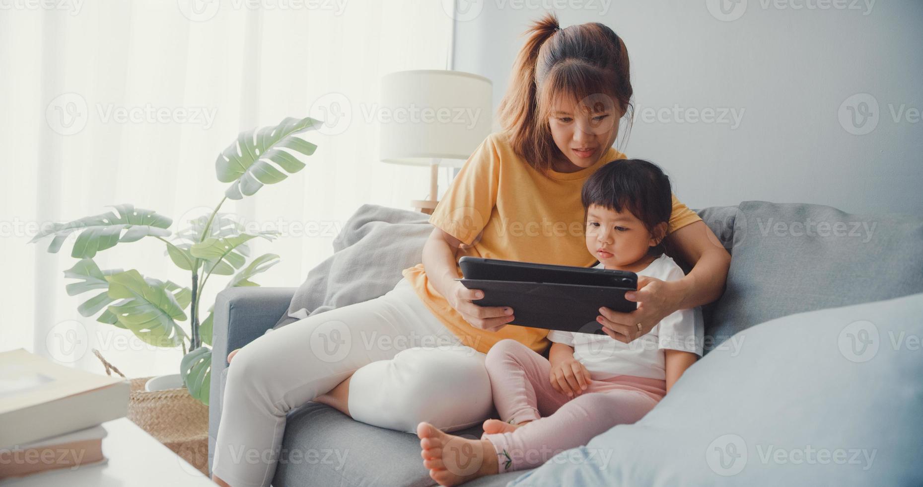 Joyeuse maman de famille asiatique joyeuse et enfant mignon utilisant un dessin animé d'intérêt pour tablette numérique et regarder un film s'amusant se détendre sur le canapé dans le salon de la maison. passer du temps ensemble, mettre en quarantaine pour le coronavirus. photo