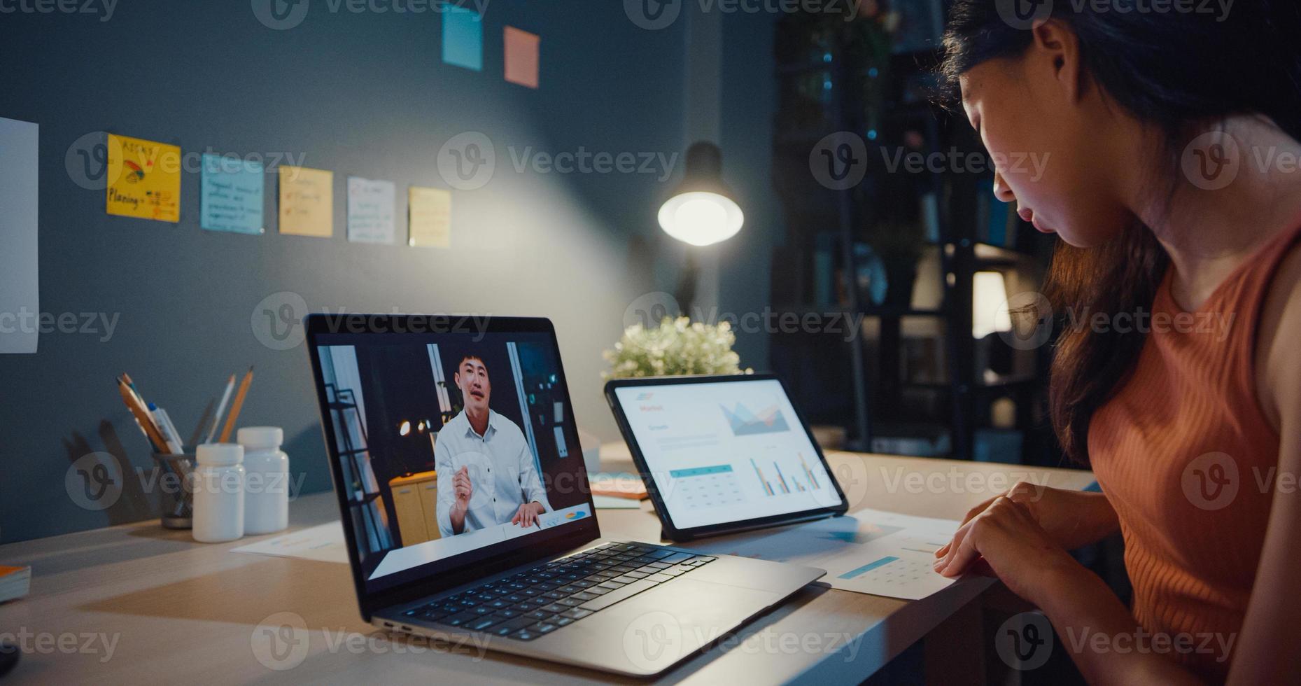 femme asiatique utilisant un ordinateur portable voir le graphique dans le tableau parler à des collègues du travail en appel vidéo tout en travaillant à domicile dans le salon la nuit. auto-isolement, distanciation sociale, quarantaine pour le coronavirus. photo