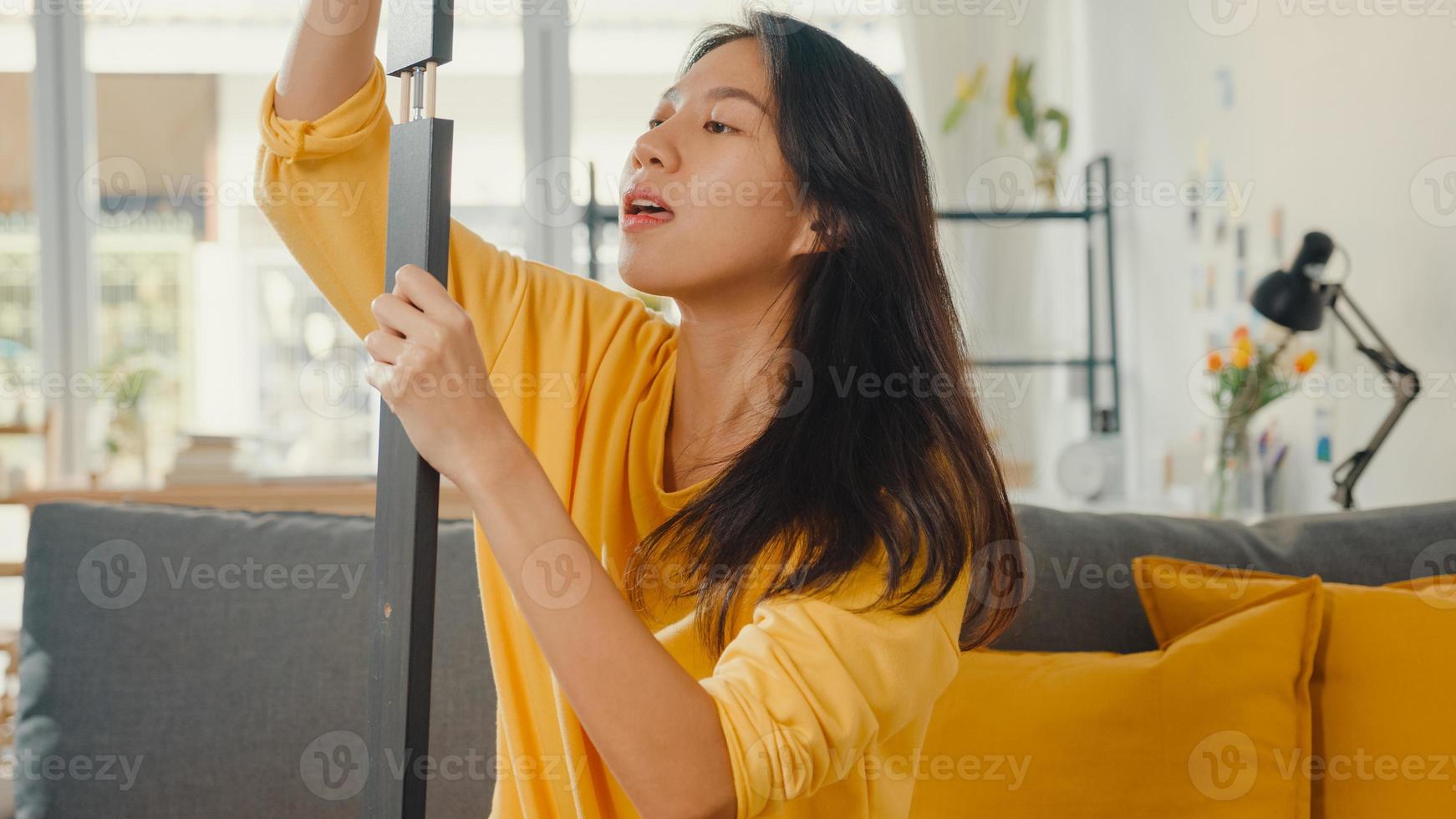 Heureuse jeune femme asiatique déballant la boîte et lisant les instructions pour assembler de nouveaux meubles décorer une table de construction de maison avec une boîte en carton dans le salon à la maison. photo