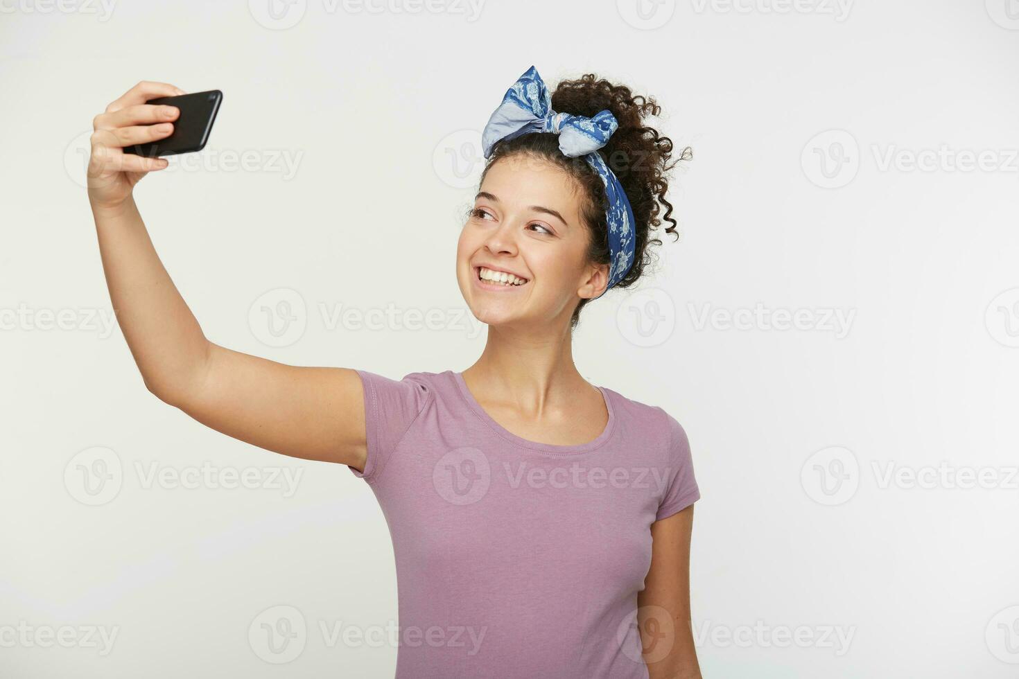 autoportrait de agréable mignonne élégant affectueux de bonne humeur charmant attrayant adorable brunette fille avec frisé cheveux dans décontractée T-shirt et Bandeau, isolé plus de blanc Contexte photo