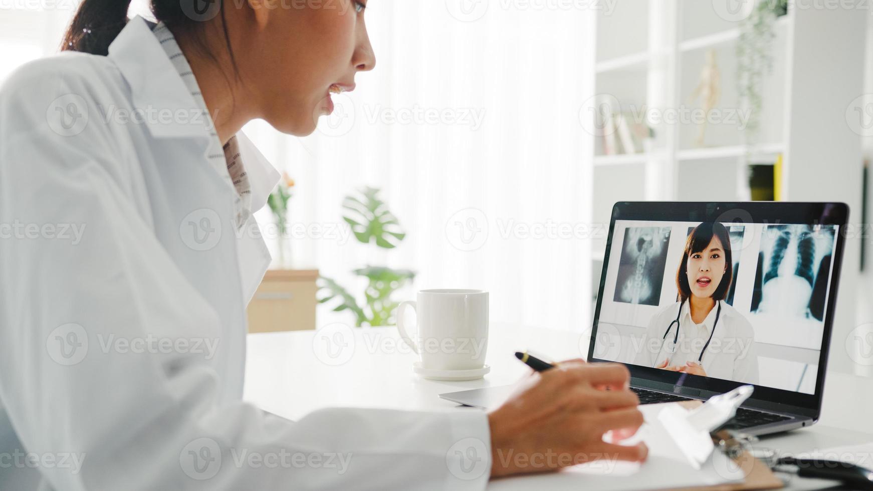 jeune femme médecin asiatique en uniforme médical blanc utilisant un ordinateur portable parlant par vidéoconférence avec un médecin senior au bureau d'une clinique de santé ou d'un hôpital. distanciation sociale, quarantaine pour le virus corona. photo