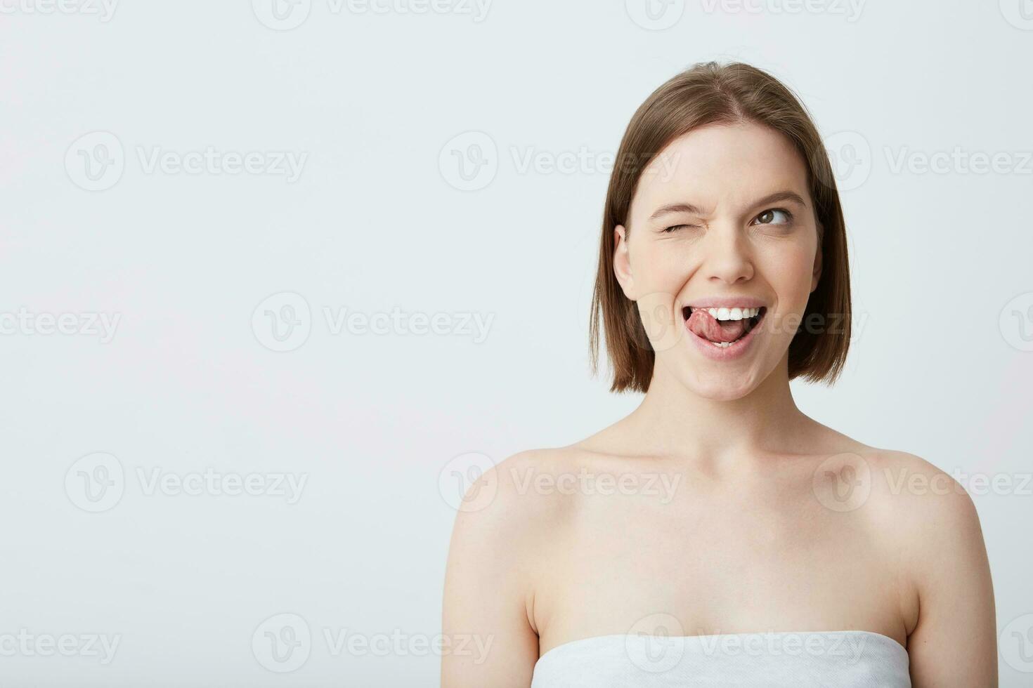 horizontal coup de attrayant Naturel Jeune femme avec foncé cheveux et parfait en bonne santé peau après douche et appliquant crème ou masque un clin d'oeil et montrant langue isolé plus de blanc Contexte photo