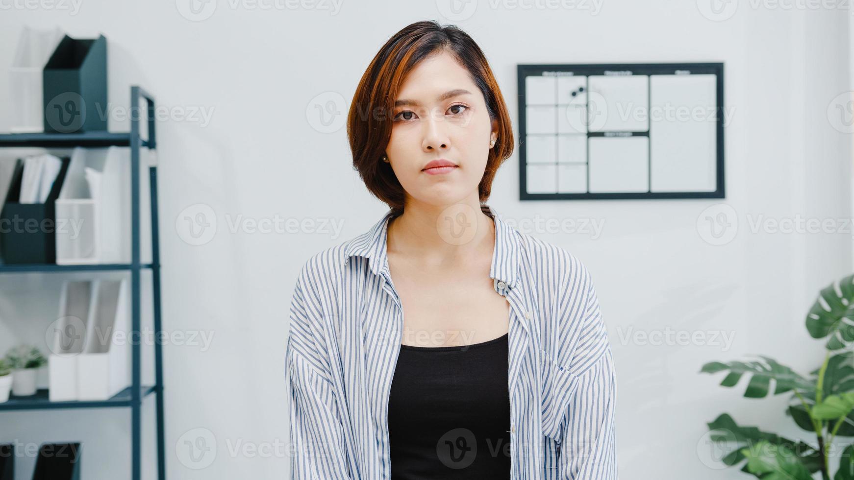 portrait de belle femme d'affaires exécutive vêtements décontractés intelligents regardant la caméra et souriant, heureux dans un lieu de travail de bureau moderne. une jeune femme asiatique parle à un collègue lors d'une réunion par appel vidéo à la maison. photo