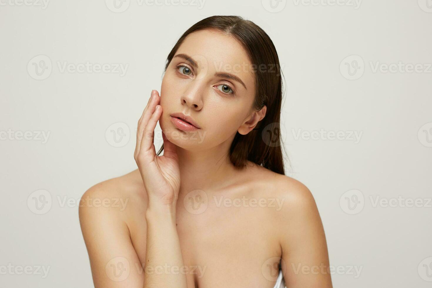 magnifique fille avec parfait en bonne santé Frais peau regards caméra comme dans le miroir, paume tendrement touche joue, soigneusement examine sa visage dans détails, tête et nu épaules photo