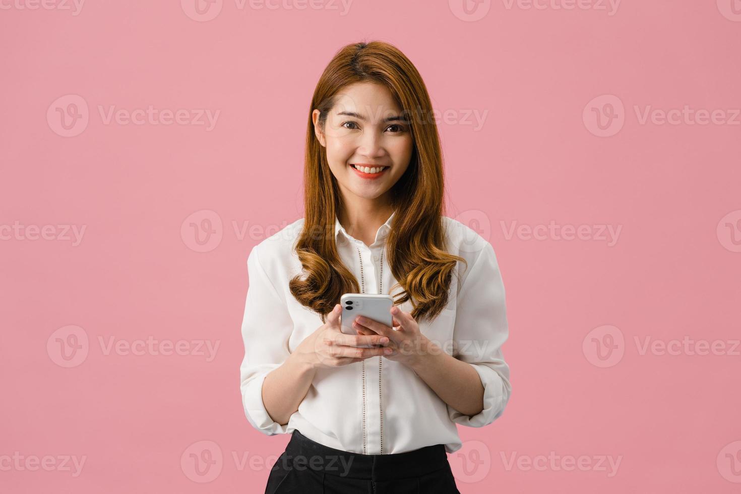 surpris une jeune femme asiatique utilisant un téléphone portable avec une expression positive, sourit largement, vêtue de vêtements décontractés et regardant la caméra sur fond rose. heureuse adorable femme heureuse se réjouit du succès. photo