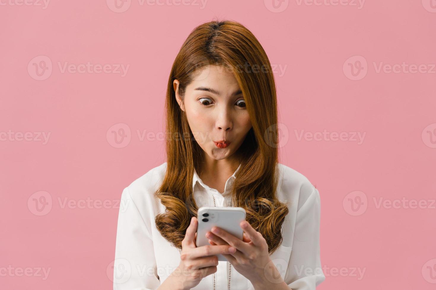 jeune femme asiatique utilisant un téléphone avec une expression positive, sourit largement, vêtue de vêtements décontractés, se sentant heureuse et debout isolée sur fond rose. heureuse adorable femme heureuse se réjouit du succès. photo