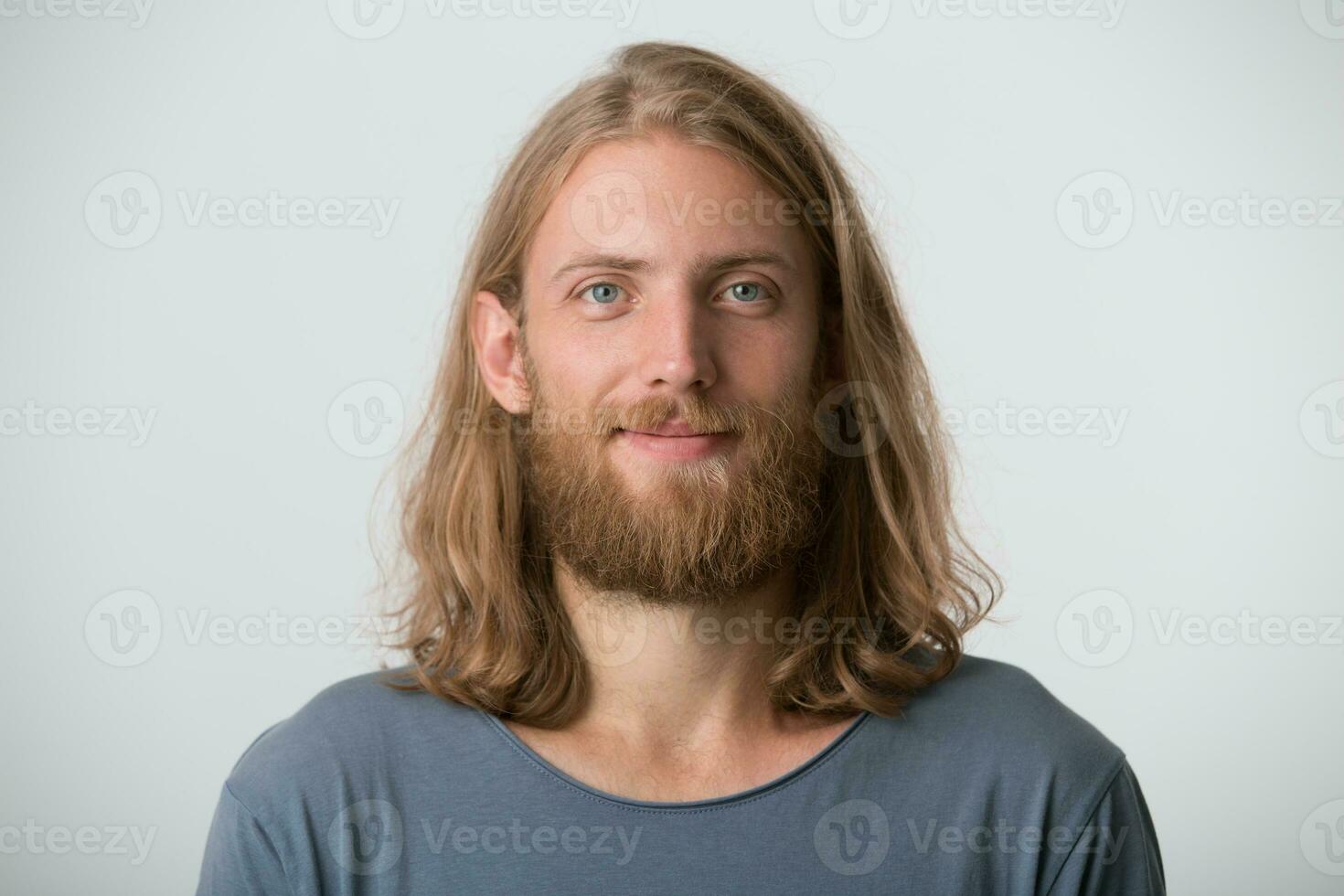 portrait de souriant Beau barbu Jeune homme avec blond longue cheveux porte gris t chemise se sent content et sur de soi isolé plus de blanc Contexte photo