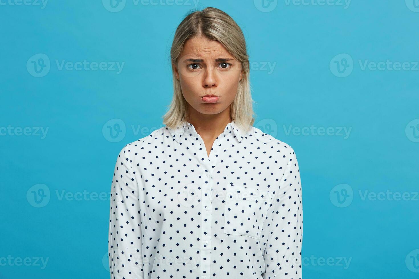 portrait de triste dérangé jolie blond Jeune femme porte polka point chemise se sent déprimé et courbure lèvres isolé plus de bleu Contexte photo