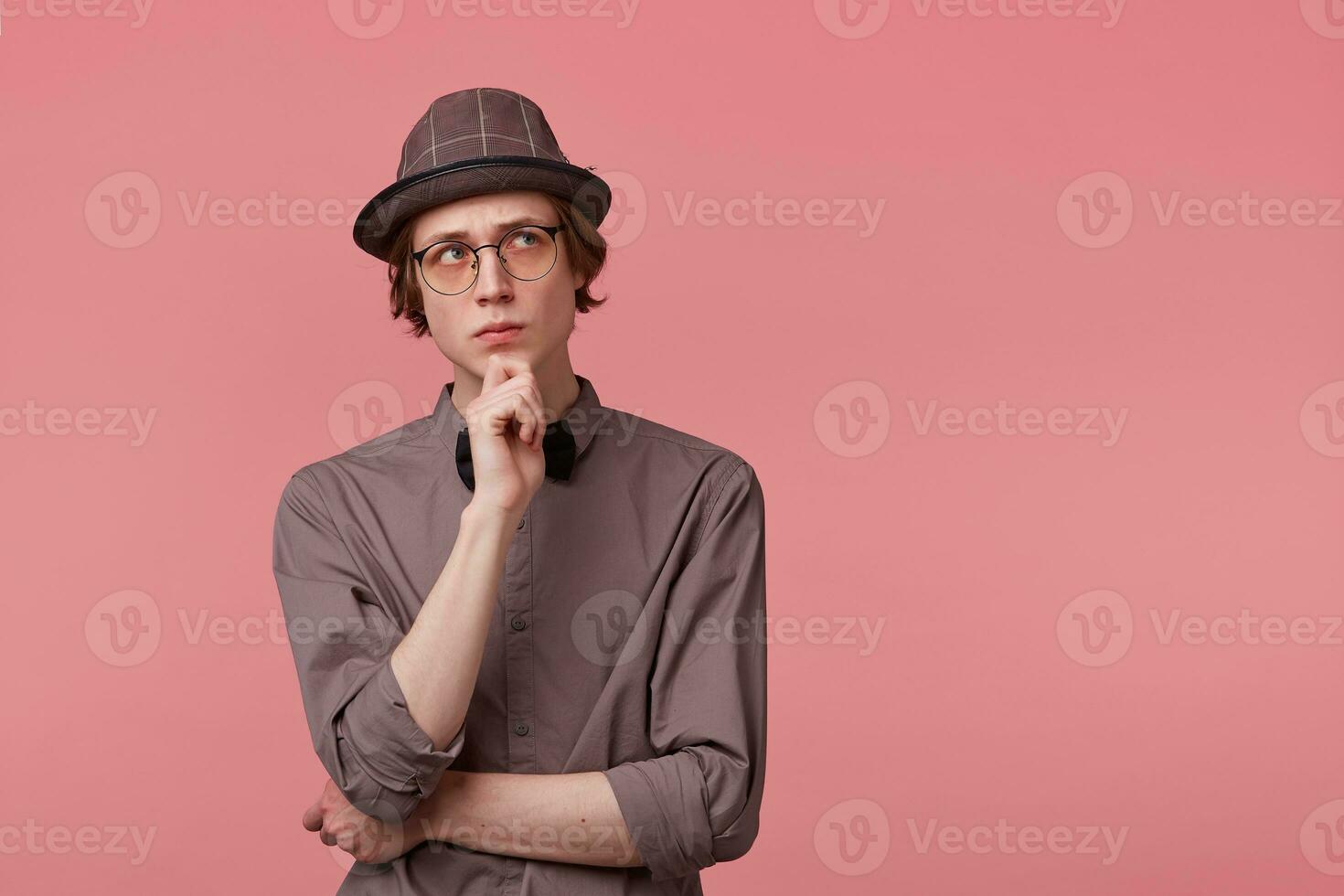 douteux Jeune intelligemment habillé gars des stands en portant le sien main sur une menton, à la recherche droite plus haut coin pensivement, inquiet, en pensant plus de une problème, effrayé de quelque chose, plus de rose Contexte photo