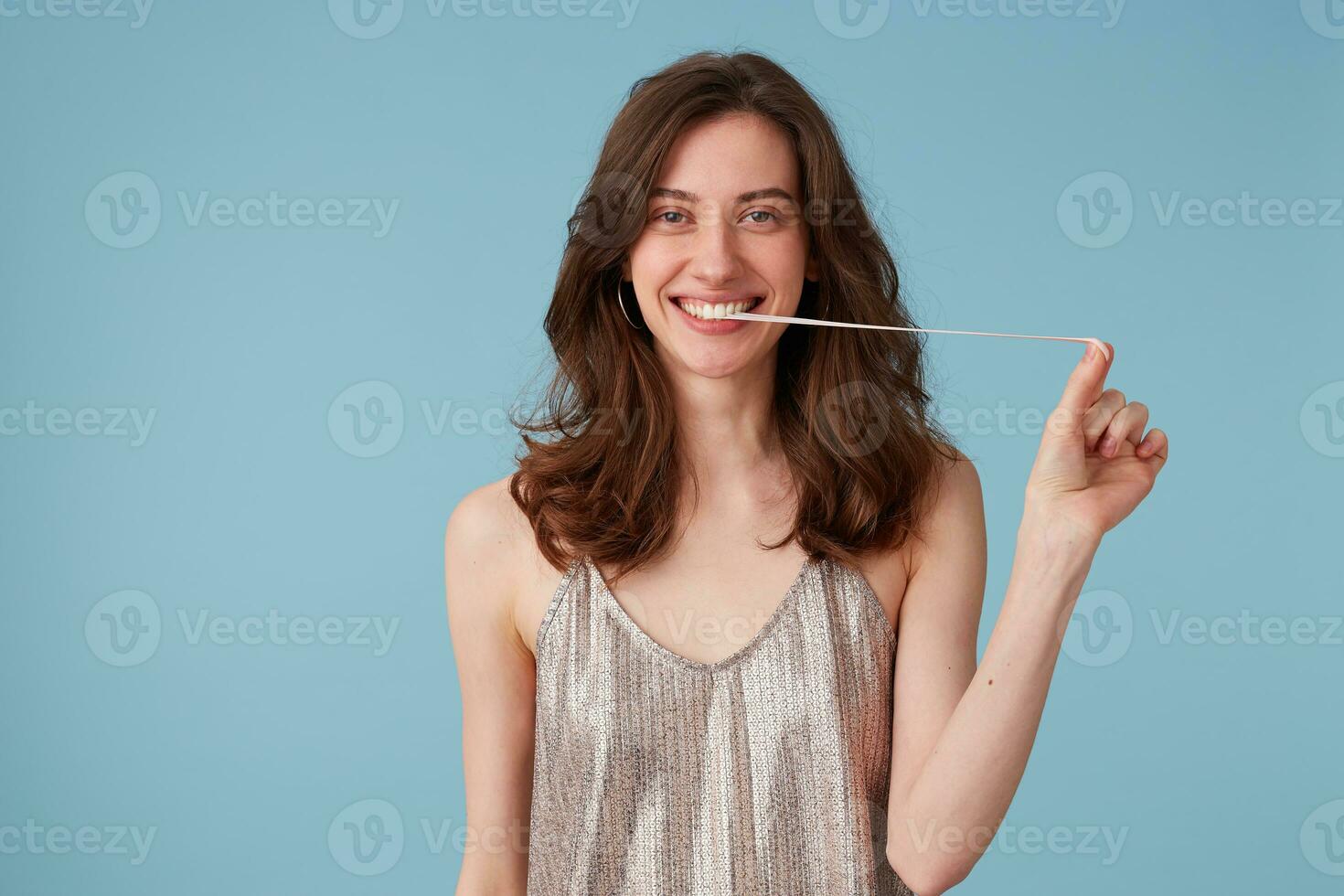 image de Jeune femme tirant gencive de sa bouche. portrait de content souriant fille mastication une gencive, ayant amusant, dans une fête robe, isolé plus de bleu Contexte photo