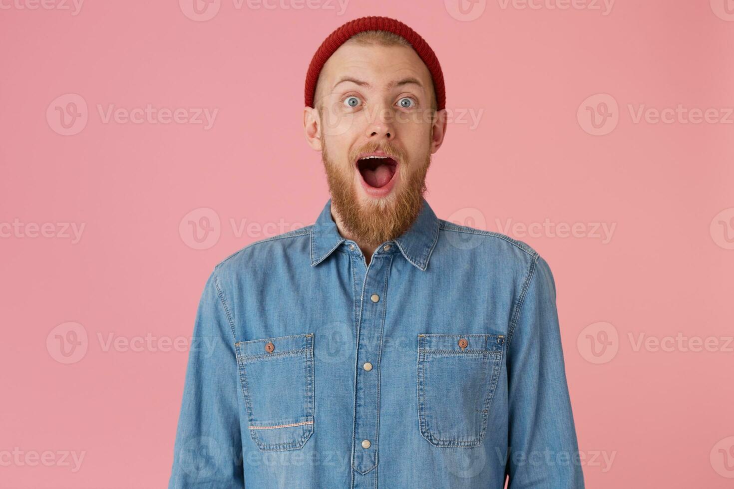 débordé avec positif émotions heureux gars dans rouge chapeau avec rouge épais barbe s'ouvre bouche largement dans excitation, chuté mâchoire, isolé sur rose mur photo