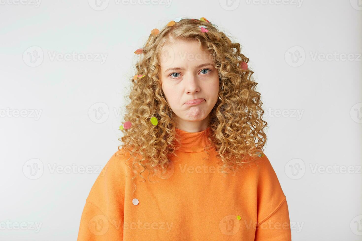 proche en haut de émotif fille regards triste, bouleversé, frustré, mécontent, exprime offense, pleurs, inférieur lèvre fit la moue, montrant sans défense, porte Orange sweat-shirt, des stands isolé plus de blanc Contexte. photo