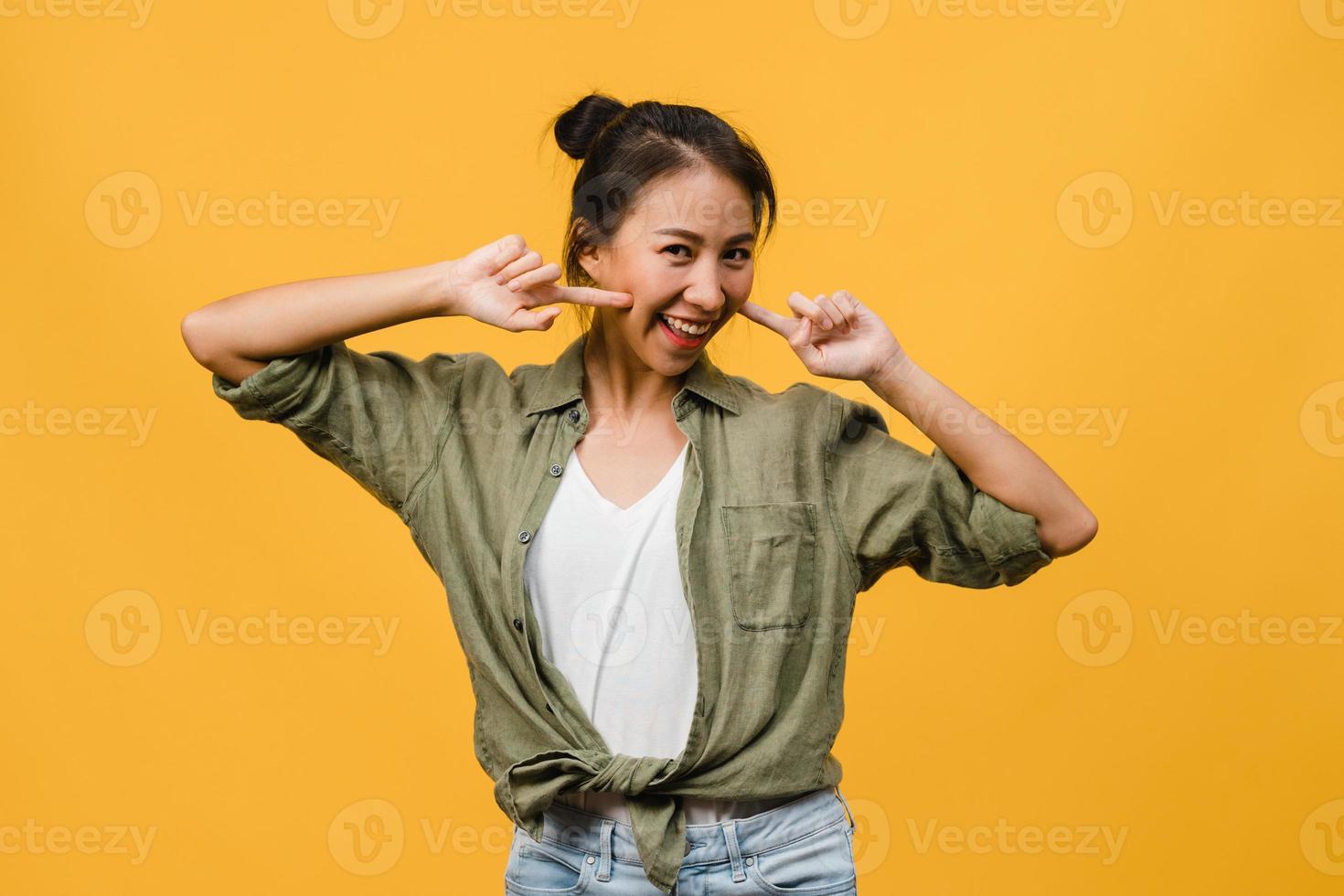 jeune femme asiatique à l'expression positive, sourire largement, vêtue de vêtements décontractés et regardant la caméra sur fond jaune. heureuse adorable femme heureuse se réjouit du succès. concept d'expression faciale. photo