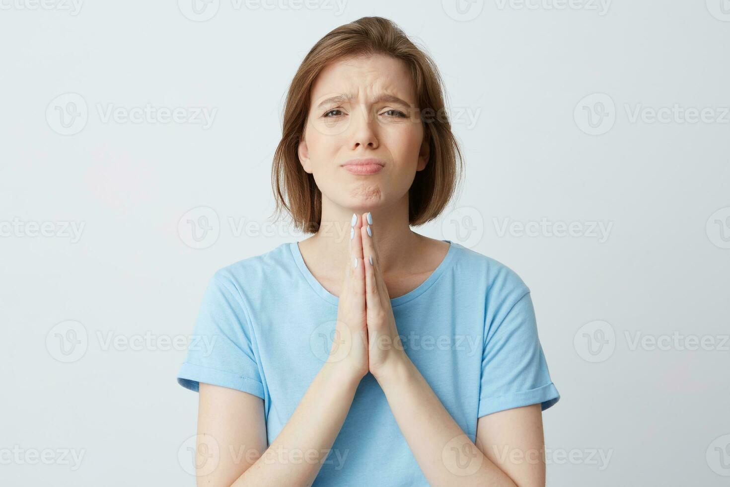 portrait de triste désespéré Jeune femme dans bleu t chemise garde mains dans prier position et demander pour Aidez-moi isolé plus de blanc Contexte photo