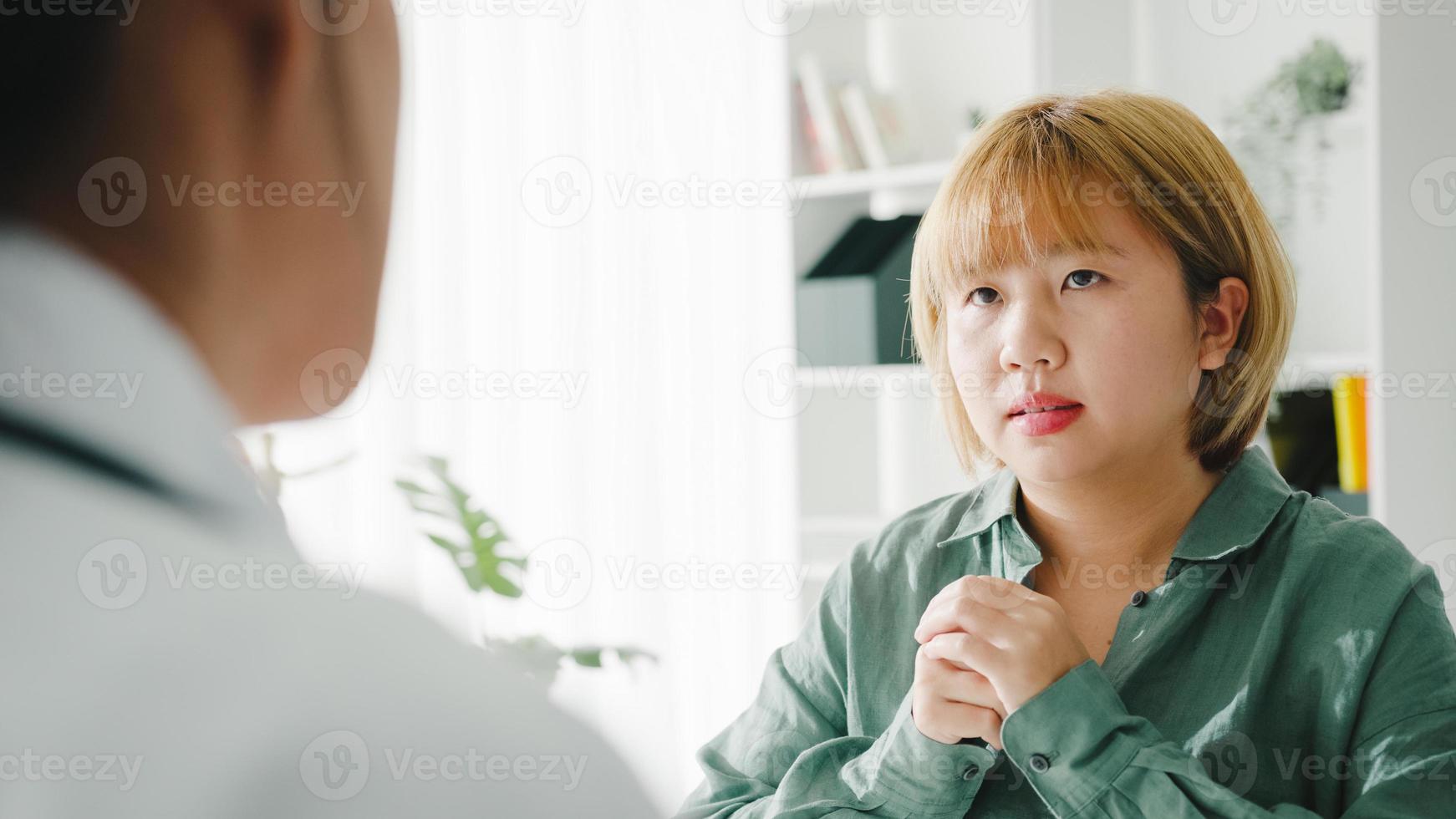 une jeune femme médecin asiatique en uniforme médical blanc utilisant un presse-papiers livre d'excellentes nouvelles discutent des résultats ou des symptômes avec une patiente assise au bureau dans une clinique de santé ou un bureau d'hôpital. photo