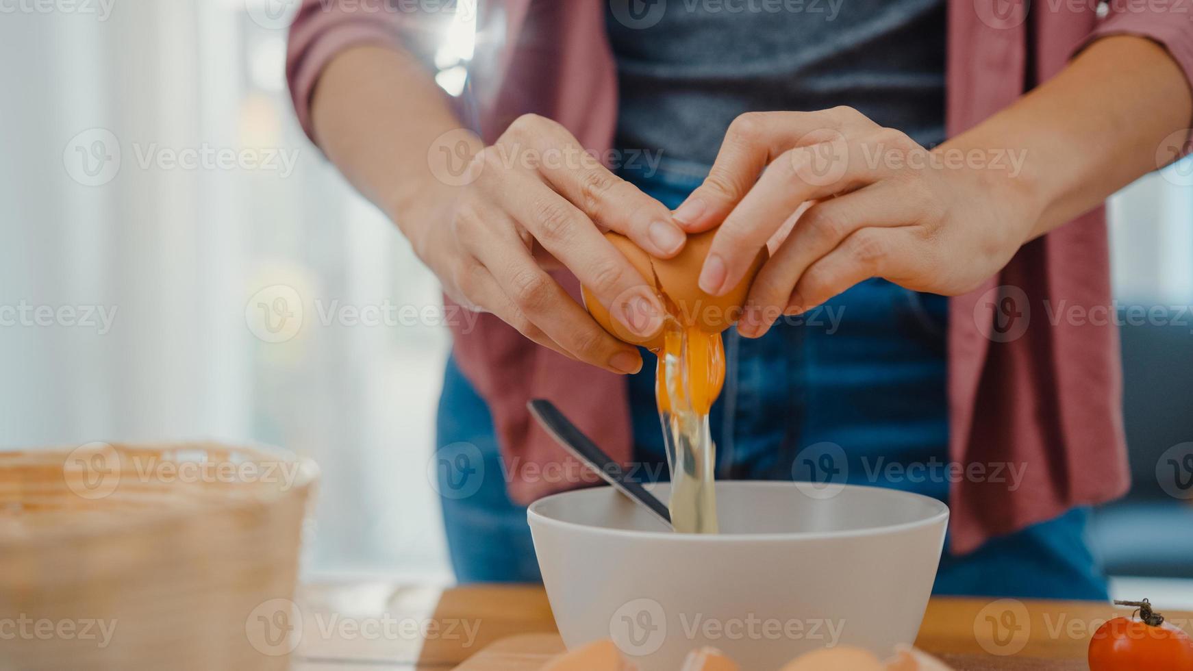 mains d'une jeune femme asiatique chef cassant des œufs dans un bol en céramique faisant cuire une omelette avec des légumes sur une planche de bois sur une table de cuisine dans la maison. mode de vie saine alimentation et concept de boulangerie traditionnelle. photo
