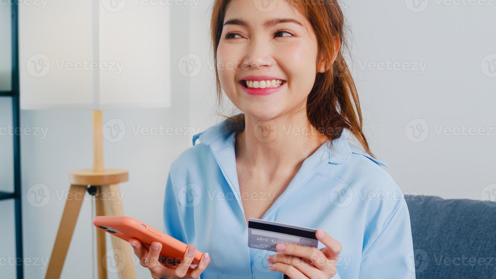 une jeune femme asiatique utilise un téléphone intelligent, achète une carte de crédit et achète un site de commerce électronique dans le salon de la maison. restez à la maison, achats en ligne, auto-isolement, distance sociale, quarantaine pour le coronavirus. photo