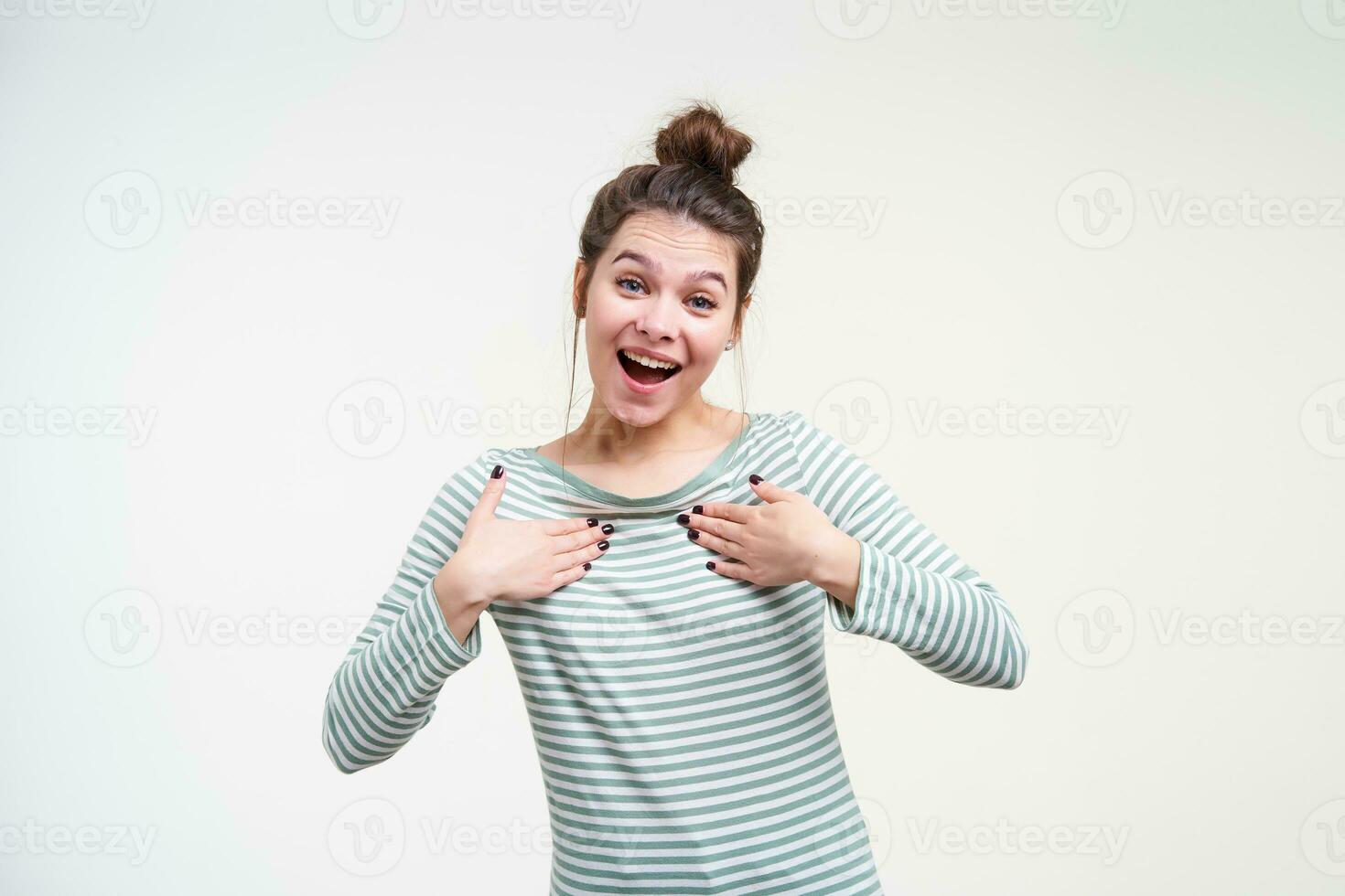 joyeux Jeune attrayant marron aux cheveux Dame avec Naturel maquillage en gardant élevé paumes sur sa poitrine tandis que à la recherche Heureusement à caméra avec large sourire, isolé plus de blanc Contexte photo