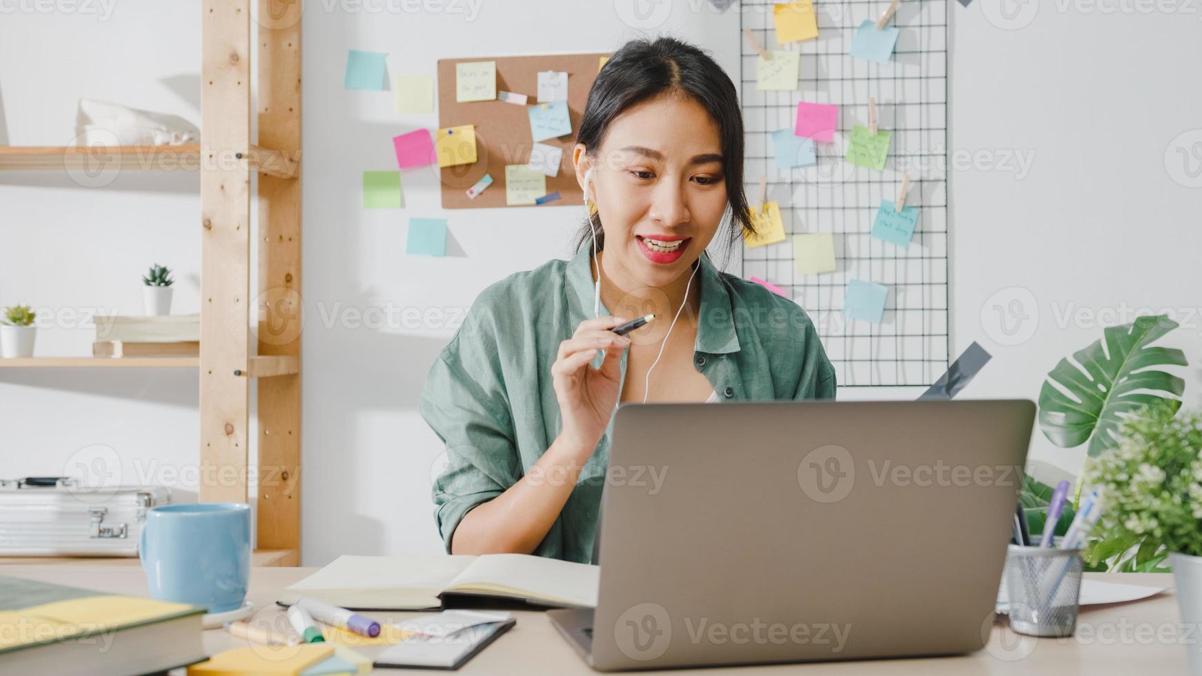 Une femme d'affaires asiatique utilisant un ordinateur portable parle à ses collègues du plan lors d'un appel vidéo tout en travaillant de manière intelligente à domicile dans le salon. auto-isolement, distanciation sociale, quarantaine pour la prévention du virus corona. photo