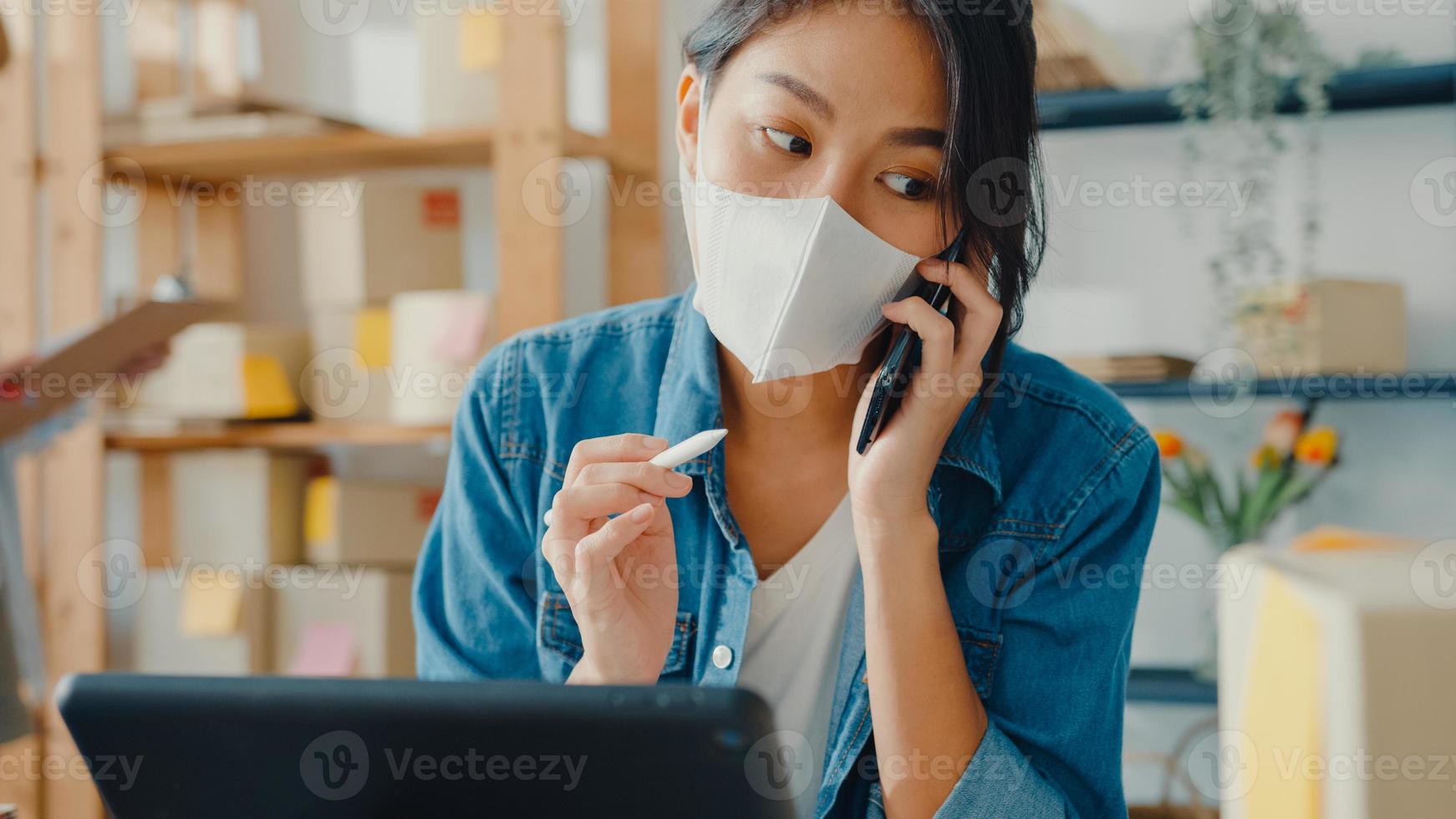 les jeunes femmes d'affaires asiatiques portent un masque facial à l'aide d'un appel téléphonique recevant la commande d'achat et vérifient le produit en stock au bureau à domicile. propriétaire de petite entreprise, concept indépendant de livraison de marché en ligne. photo