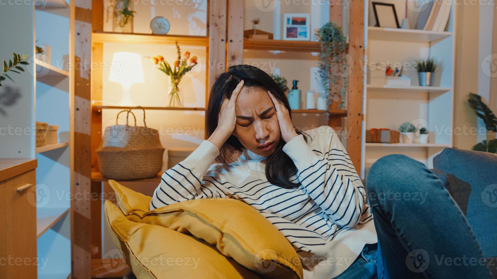 une dame asiatique réfléchie souffrant d'insomnie s'assoit sur un canapé dans le salon la nuit à la maison avec une sensation de solitude, une adolescente triste et déprimée passe du temps seule à la maison, à distance sociale, quarantaine de coronavirus. photo