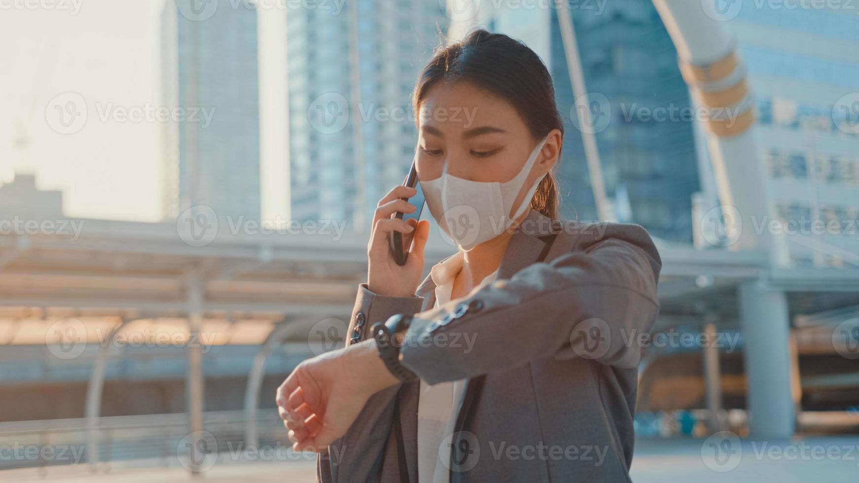 jeune femme d'affaires asiatique en vêtements de bureau de mode porte un masque médical parle par téléphone tout en marchant seule en plein air dans une ville urbaine. affaires en cours, distanciation sociale pour empêcher la propagation du concept covid-19. photo