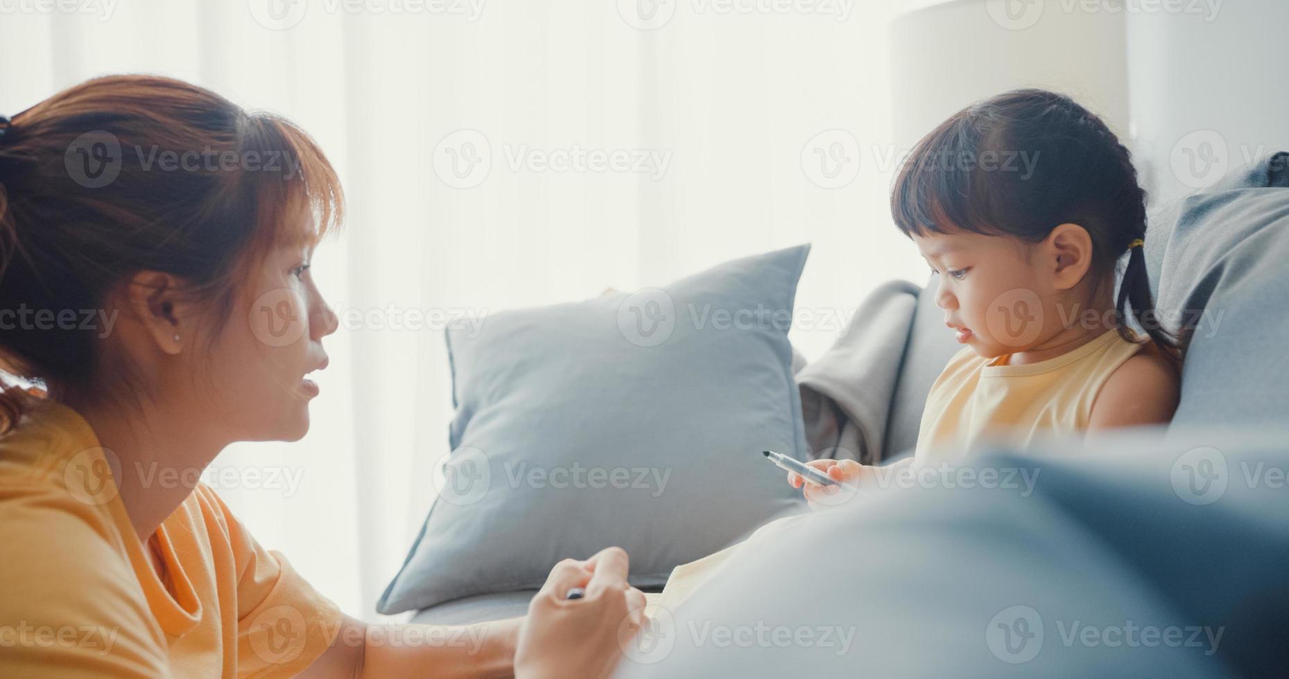 Joyeuse famille asiatique joyeuse, maman apprend à une fille à utiliser un album de peinture et des crayons colorés s'amusant à se détendre sur un canapé dans le salon de la maison. passer du temps ensemble, distance sociale, quarantaine pour le coronavirus. photo